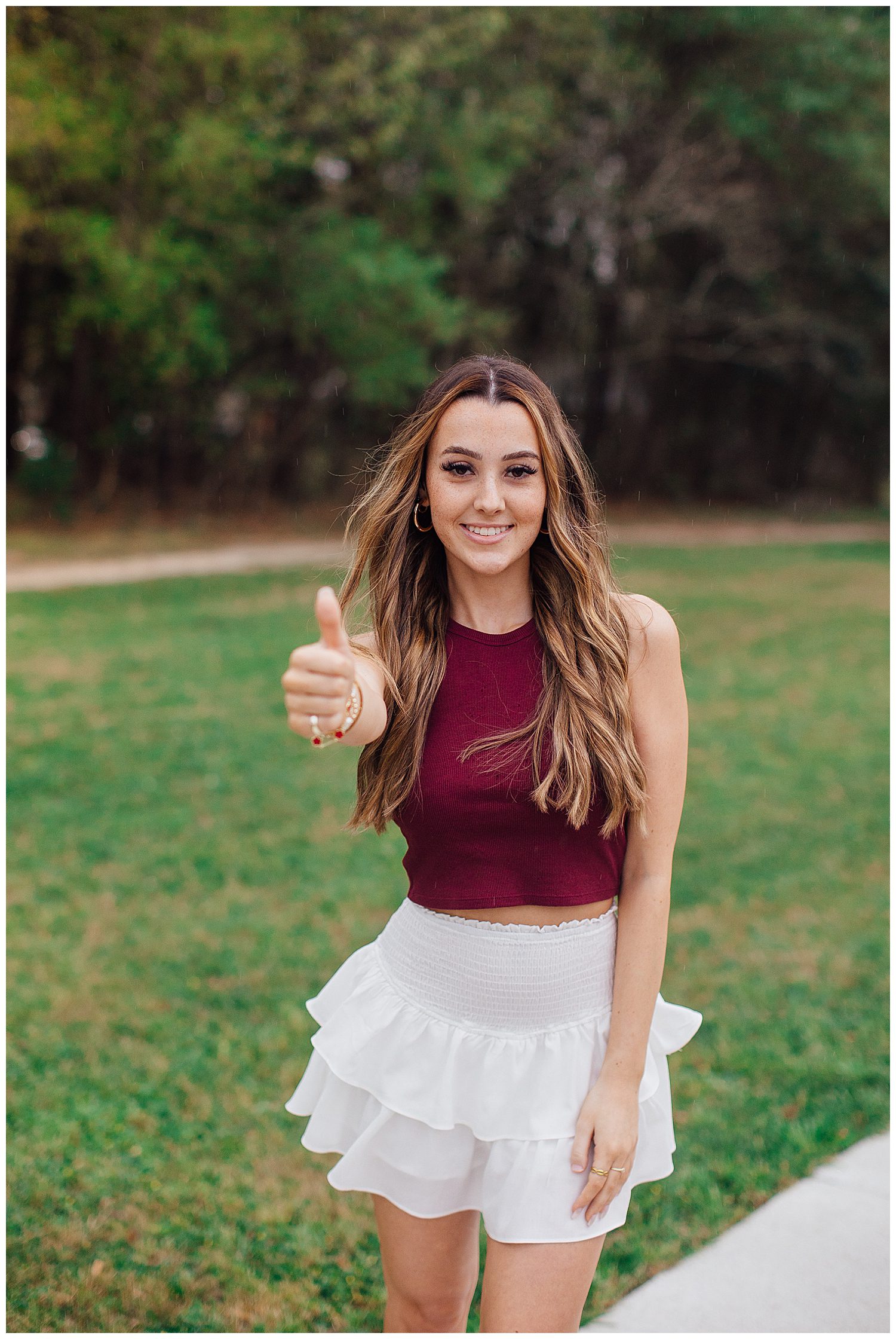 closeup image of high school senior girl in white skirt and maroon shirt holding thumb up