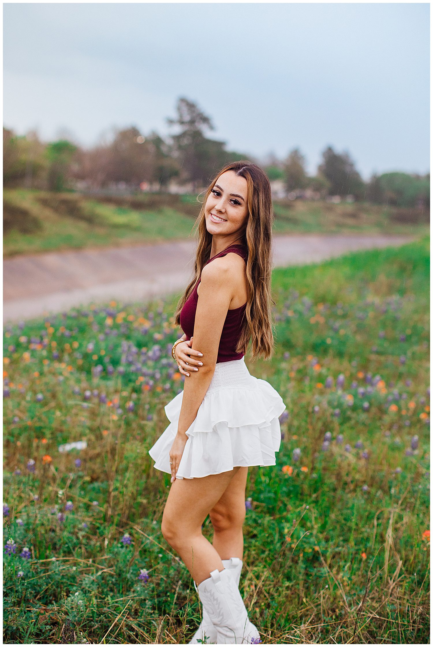 high school senior in white skirt and maroon shirt standing in Houston bluebonnet field