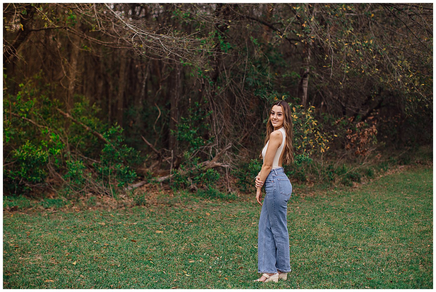 high school senior portrait of girl in denim jeans and beige top standing in field Houston