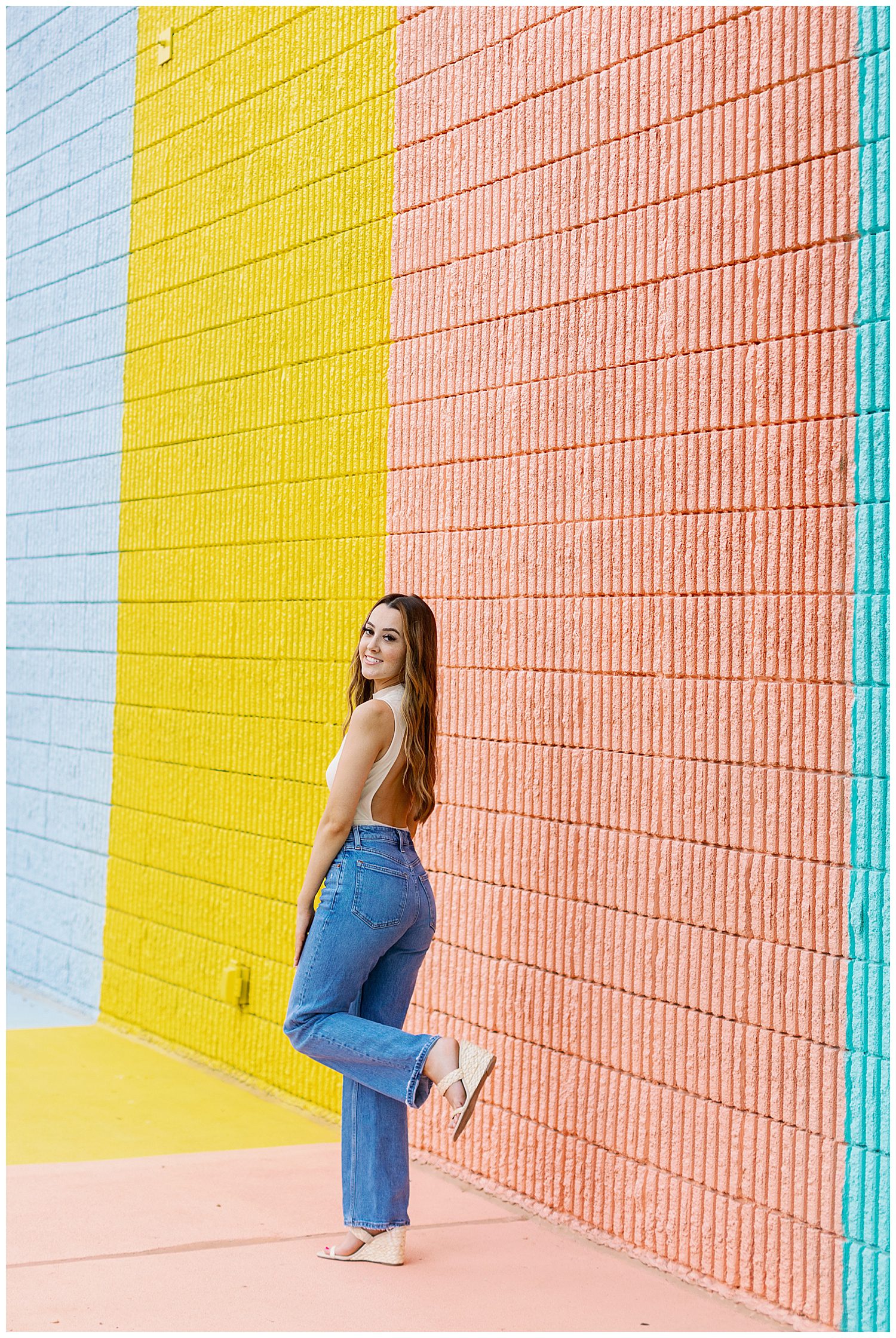 girl in denim jeans and beige unitard kicking heel up for sugar and cloth color wall portraits outdoors Houston