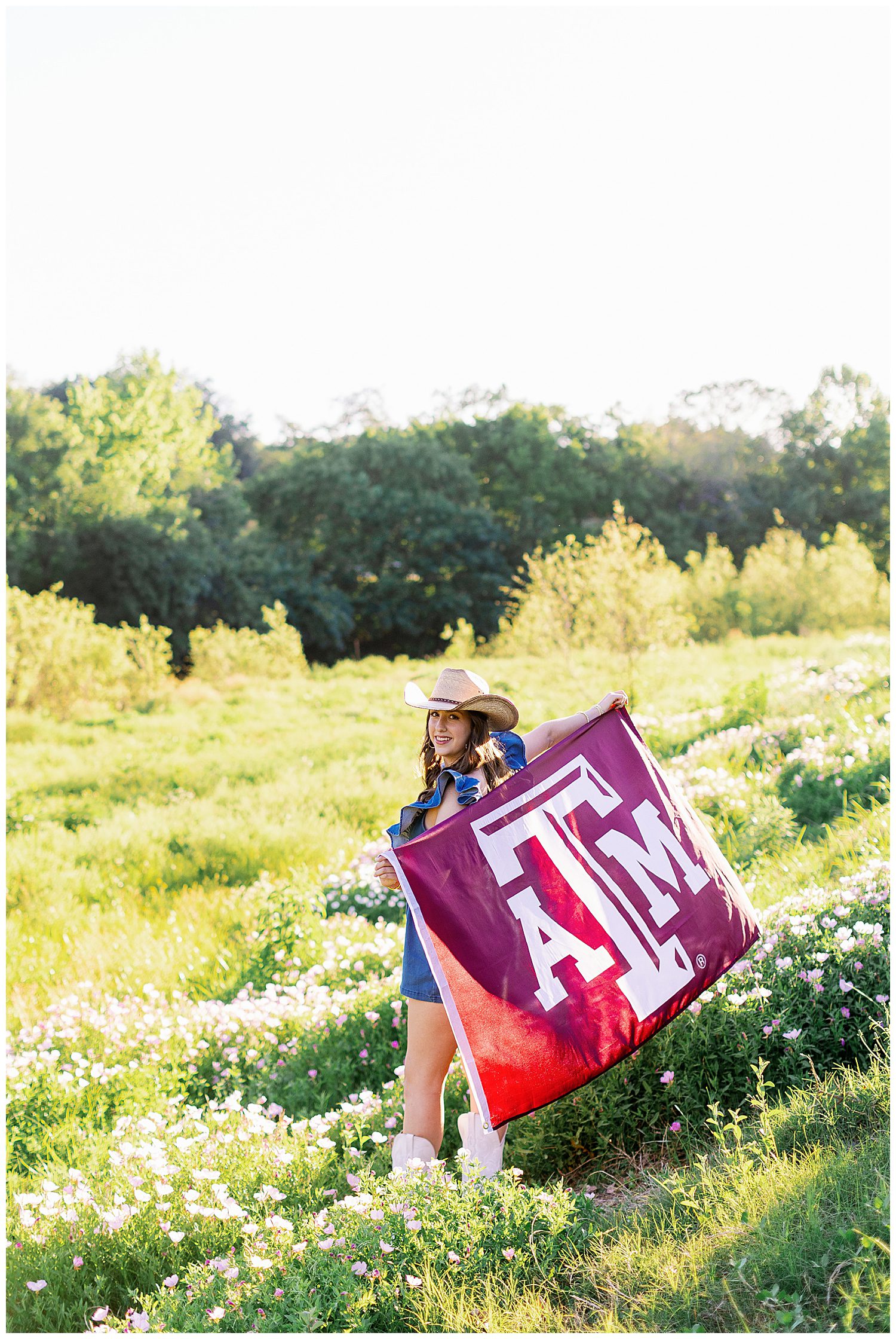 college flag senior pictures with girl in denim romper and brown boots standing in field with flag behind her back